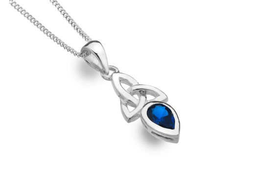 A silver necklace on a fine chain with a knotted pendant that has a dark blue teardrop gem coming off the bottom