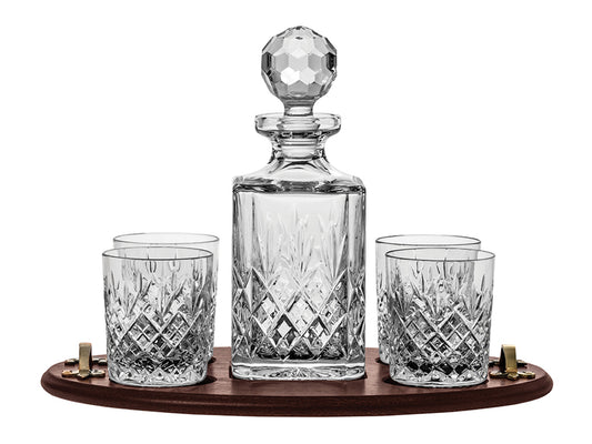 A crystal decanter set with four matching tumblers, all with the same cut pattern on the outside, sitting on a brown wood tray with gold handles that is included in the set.