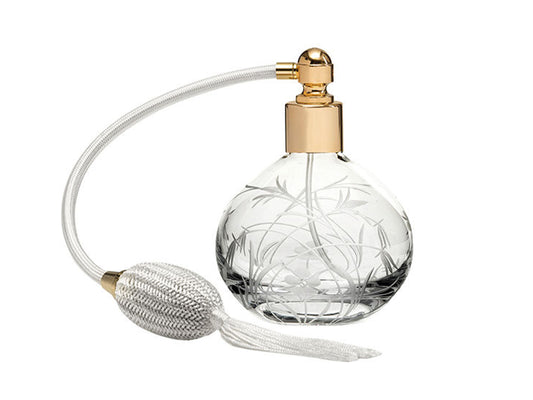 A round crystal perfume bottle with a gold lid and a cream atomiser. It has a wildflower design cut into the exterior, giving a frosted effect.