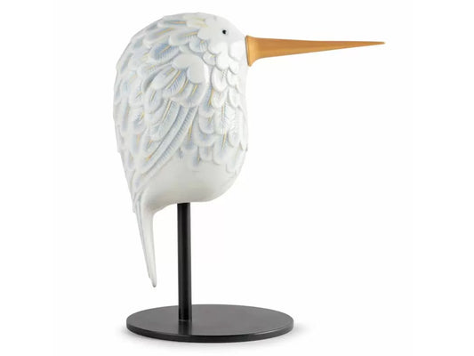A white porcelain figure of an abstract hummingbird with intricately carved feathers on one side, then a flat black painted feather pattern on the other. It has a gold beak.