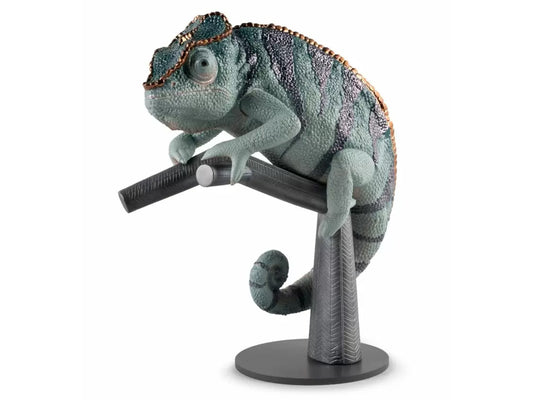 A green, blue and grey chameleon with metalic copper highlights, perched on a grey lacquered stand that emulates a branch