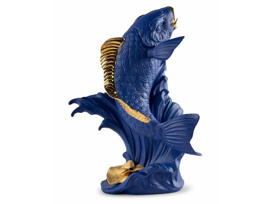 A bright blue sculpture of a koi fish leaping out of a wave made of matte porcelain, featuring gold lustre highlights on the fish's fins and tail