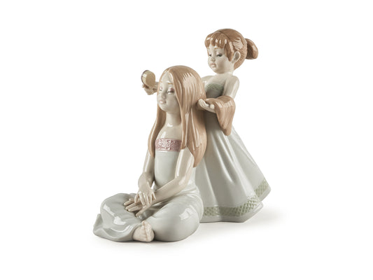 A porcelain figure of two young girls in pastel greens and pinks, with one seated and the other standing behind her to brush the seated girl's hair