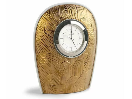 An oval clock with a flat base, carved with intricate flame designs and finished with a gold lustre on the white porcelain body.