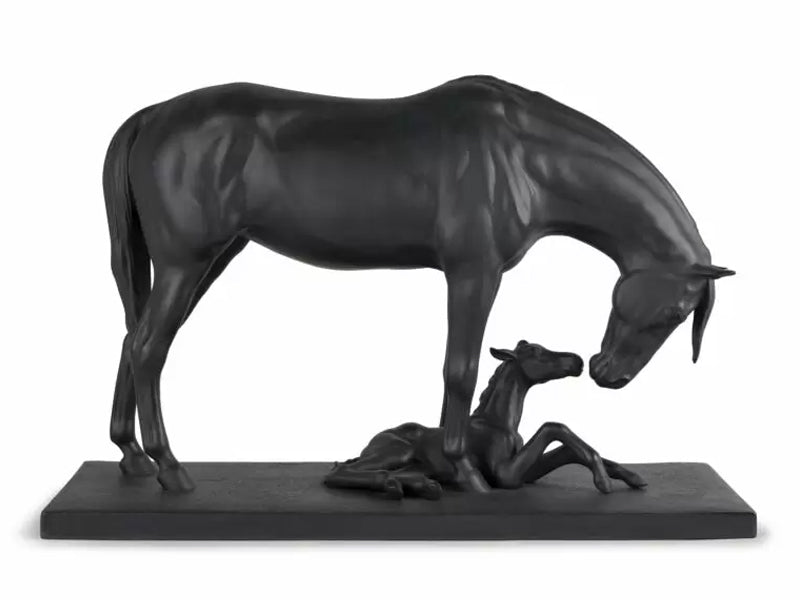 A matte black figure of a mother and baby horse. The mother stands over the foal, who is lying between her front legs. Their necks are bent so that their muzzles almost meet.