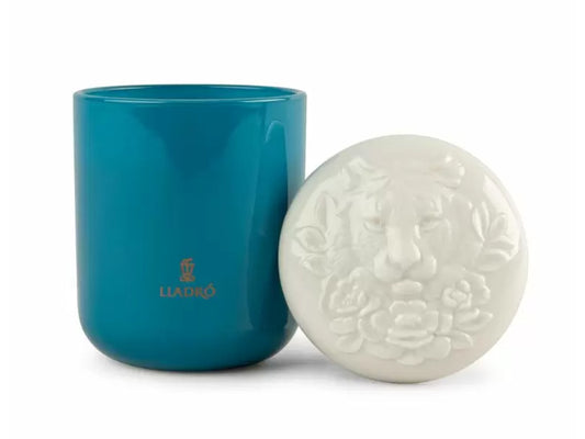 A deep blue glass candle in a jar with a white porcelain lid with a tiger's face and flowers carved into it.