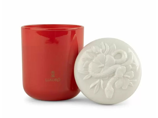 A deep orange glass glass candle with a white porcelain lid with an intricate floral design with a snake looping through the centre