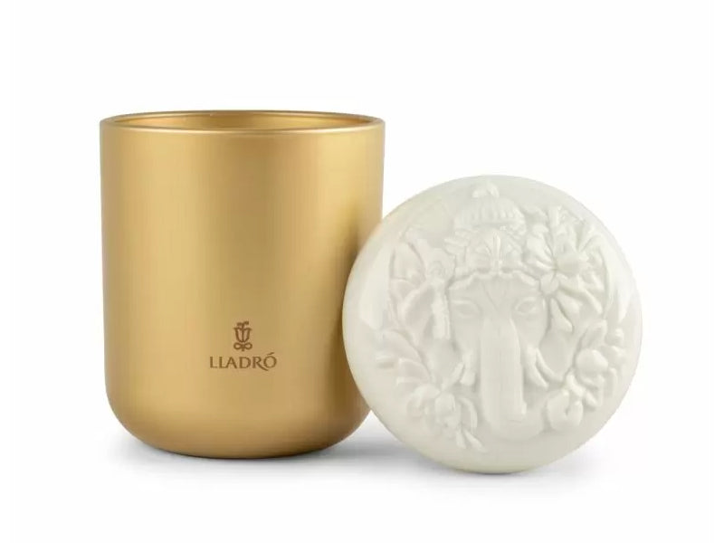 A gold glass candle with a white porcelain lid engraved with the likeness of Lord Ganesha