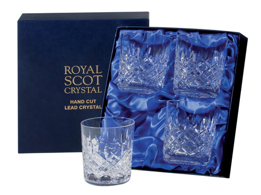 A set of four large tumblers in a navy blue silk-lined presentation box. The glasses have a cut design engraved on each one, featuring a bed of diamonds at the base, topped with single flicks reaching up towards the smooth rim. There is gold branding on the lid of the box.