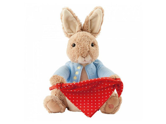 A soft plushie teddy of Peter Rabbit, the beloved character from Beatrix Potter's tales. Peter Rabbit is depicted wearing his iconic blue waistcoat adorned with gold buttons. He holds a polka-dot red handkerchief that moves up and down playfully during a game of peek-a-boo. The plushie's fur is a gentle shade of brown. At the bottom of its foot, there is an on and off button for interactive fun.