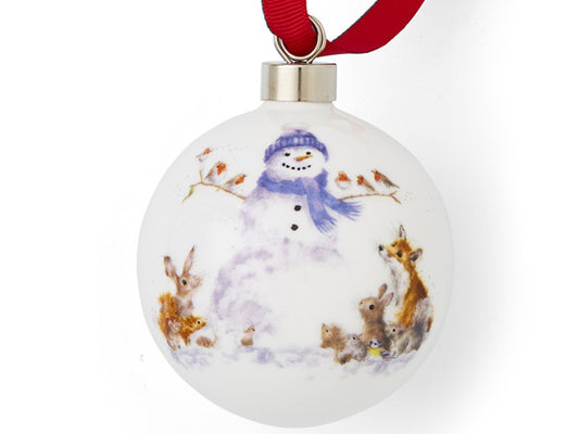 A white porcelain bauble with a snowman surrounded by small animals on it, hung off a red ribbon