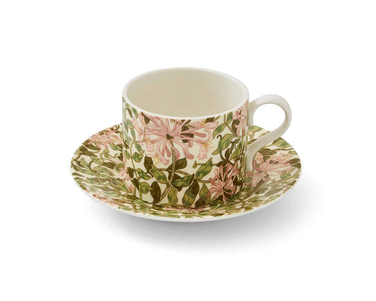 A matching porcelain teacup and saucer featuring the popular design from May Morris called Honeysuckle. The pattern features winding vine leaves and small flowers, resembling the shape of a honeysuckle plant. The flowers are depicted in shades of pink with white accents with a golden centre where the plant holds its pollen.