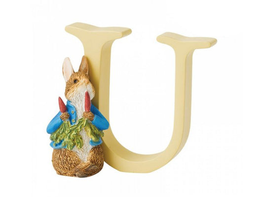 A pastel yellow capital letter U with Peter Rabbit standing against the left side, eating radishes in his blue jacket