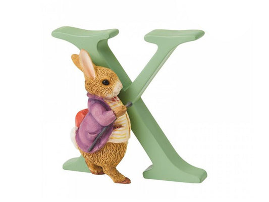 A sage green capital letter X with a brown bunny walking in front of it, wearing a purple jacket and carrying a cane and knapsack