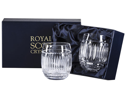 A pair of gin and tonic tumblers with an art deco pattern around the outside that is made up of vertical panels with a smooth rim. they come in a navy-blue silk-lined presentation box with gold branding on the lid.