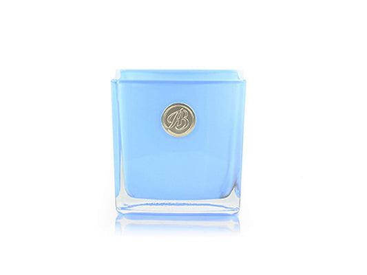 A blue scented candle in a glass votive with a gold logo on one side