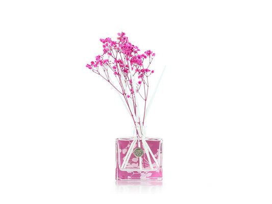 A glass bottle with a bright pink floral design, with white reeds and pink dyed dried gypsophila in it