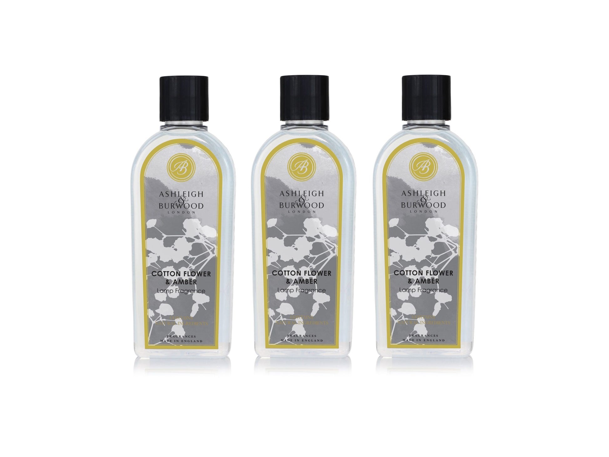 Three bottles of lamp fragrance liquid in a cotton-flower and amber scent.. The bottles are clear with floral grey labels and black lids.