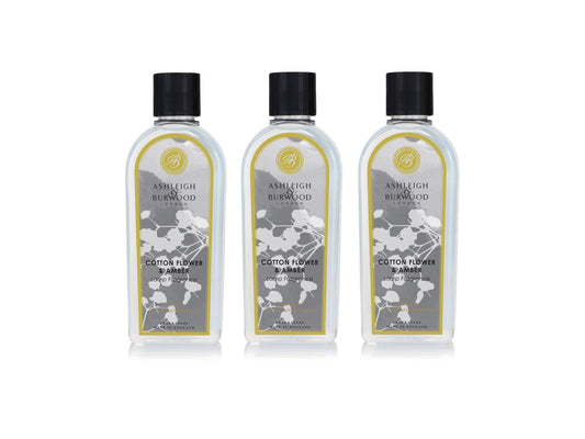 Three bottles of lamp fragrance liquid in a cotton-flower and amber scent.. The bottles are clear with floral grey labels and black lids.