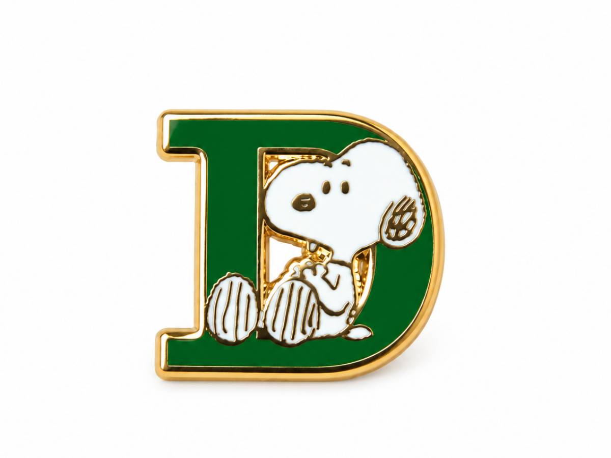 A green enamel letter D pin featuring the character Snoopy sitting inside, with gold-tone metal outlines and white enamel details, shown on a plain white background.