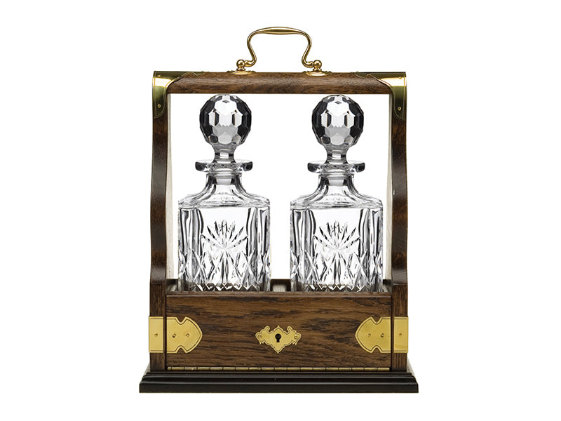 Two crystal decanters with a cut design and round stoppers inside an oak tantalus with gold hardware