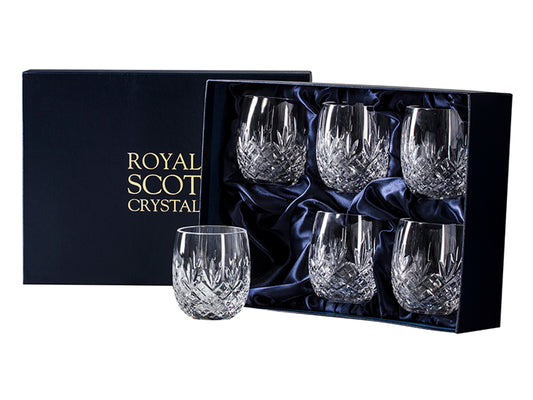 A set of six crystal barrel tumblers with an Edinburgh cut, with a bed of diamonds around the base and a triple-pointed fan pointing up towards the smooth rim. They come in a navy-blue silk-lined presentation box with gold branding on the lid.