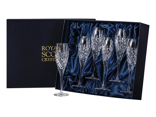 A set of six matching champagne flutes with a bed of diamonds cut above the stem, with a three-pointed fan sitting above it with a smooth rim. They come in a navy-blue silk-lined presentation box with gold branding on the lid.