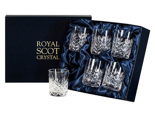 A set of six crystal whisky glasses with a cut design, featuring a bed of diamonds around the base and a three-pointed fan pointing up towards the smooth rim. They come in a navy-blue silk-lined presentation box with gold branding on the lid.