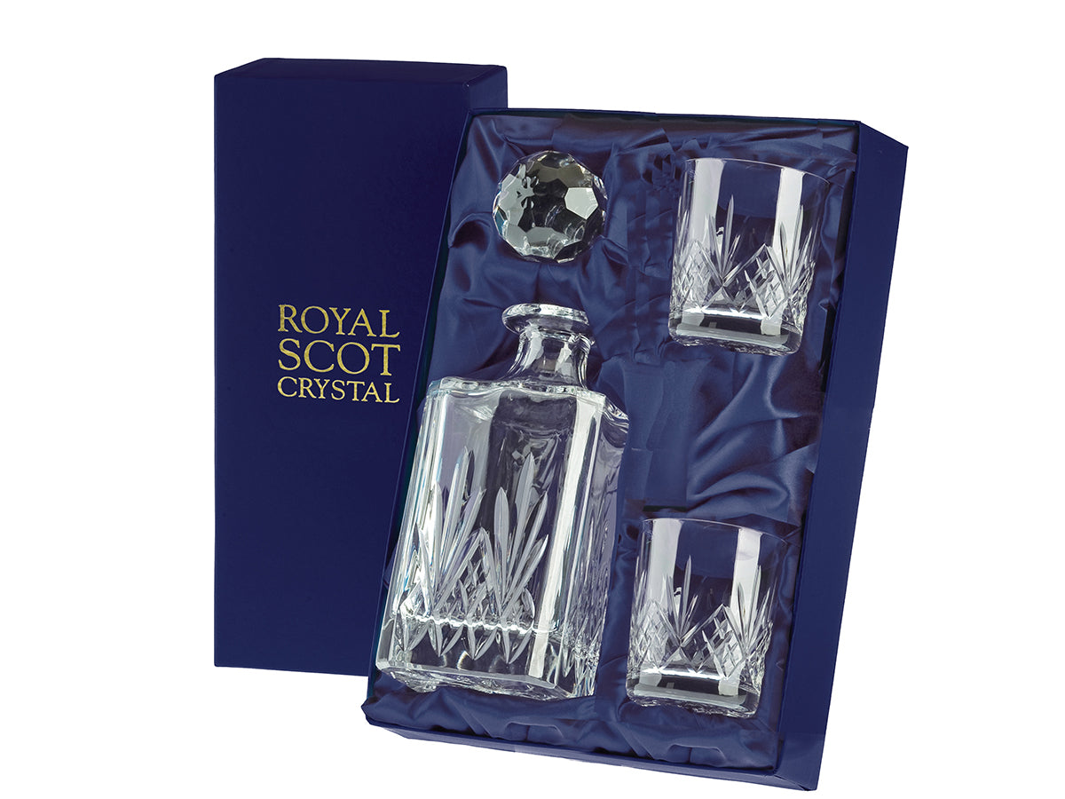 A square spirit decanter and two matching whisky glasses with a highland cut consisting of a bed of diamonds around the base of each piece, topped with a five-pointed fan and smooth tops. The set comes in a navy-blue silk-lined presentation box with gold branding on the lid.