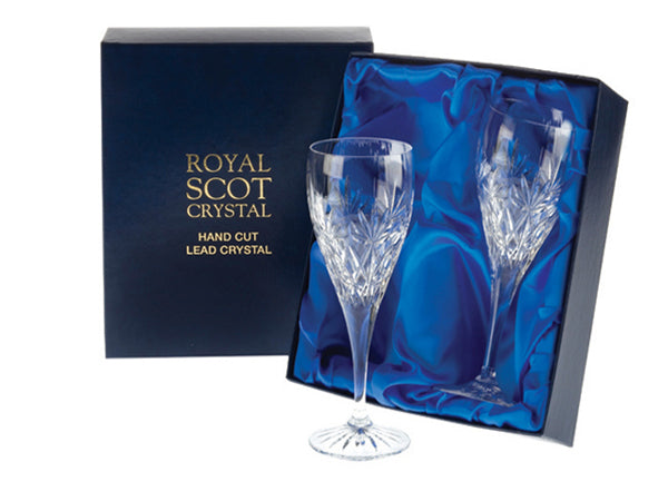 A pair of stemmed dessert wine glasses with diamonds cut above the stem, topped with a seven-pointed fan and a smooth rim. They come in a navy-blue silk-lined presentation box with gold branding on the lid.