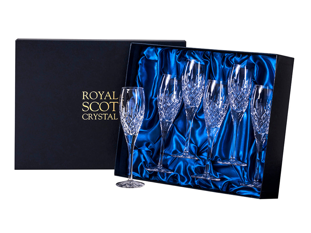 A set of six matching champagne flutes in a navy blue presentation box. Each flute is cut with a London design, which is a bed of diamonds at the base of the flute's body with single flicks reaching up towards a smooth rim.