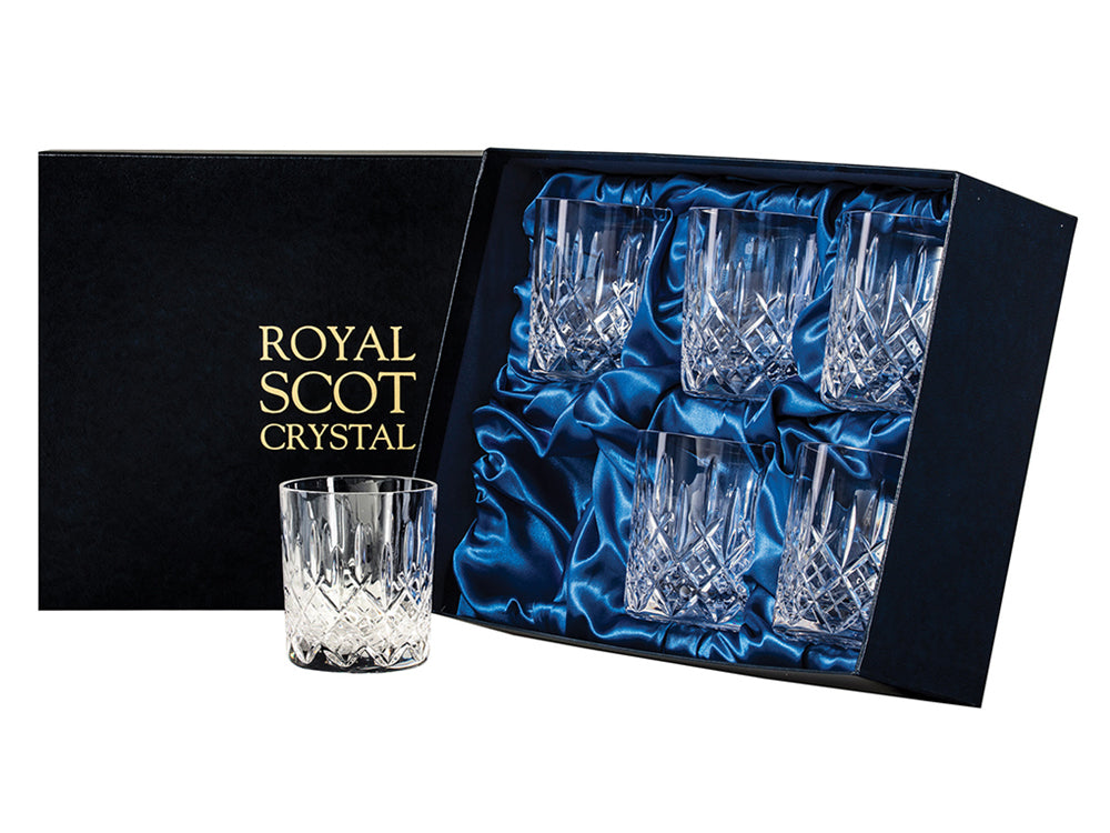 A set of six large whisky glasses with a hand-cut design on the exterior, presented in a navy blue silk-lined box with gold branding on the lid. the cut on the glasses is a bed of diamonds with single flicks reaching up towards the smooth rim.