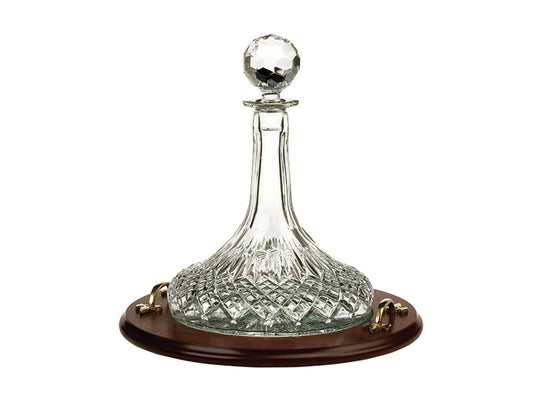 A crystal ships decanter with a wide base and long neck and round stopper, sitting on a dark wood tray with gold handles