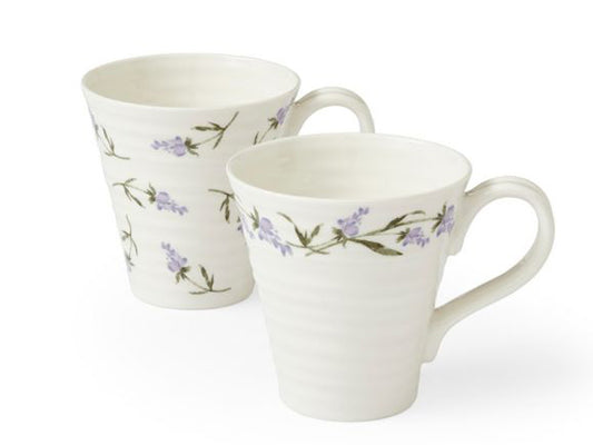 A set of two Sophie Conran mugs that have been designed with her staple ripple effect and printed with individual lavender patterns. One has a chain of lavender printed around the upper outer rim of the mug, whilst the other has lavender sporadically printed all across its exterior.