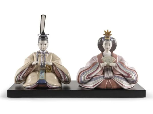 A pair of hina dolls in intricate robes on a dark wood plinth