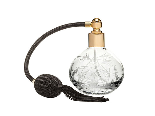 A round crystal perfume bottle with a gold lid and black atomizer. The bottle has a wildflower pattern cut into the outside