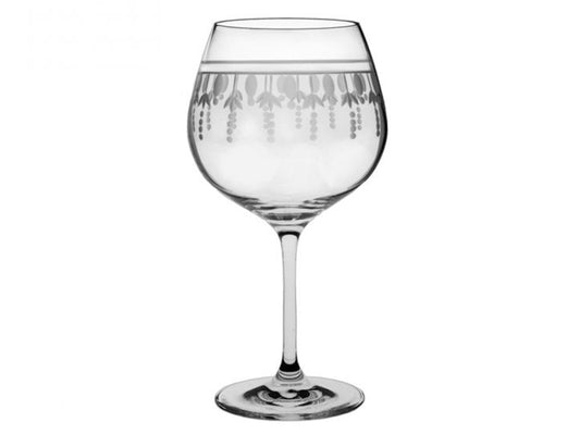 A gin copa glass with an ornate pattern cut into the outside, with a band around the rim and dashes going down towards the base