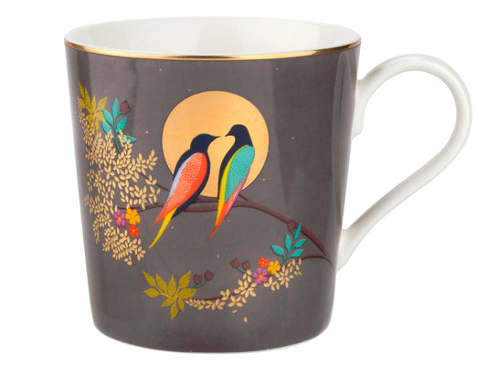 A porcelain mug with a dark grey background, featuring two exotic birds perched on a leafy branch, outlined by a gold moon