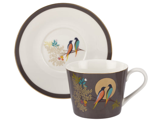 A matching tea cup and saucer set with a dark grey rim / background and gold leaves, featuring two birds in bright colours in the centre