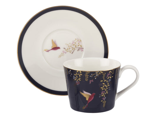 White porcelain tea cup and saucer with navy rim and background. It has a hummingbird design and honeysuckle vines, all embellished with fine gold details,