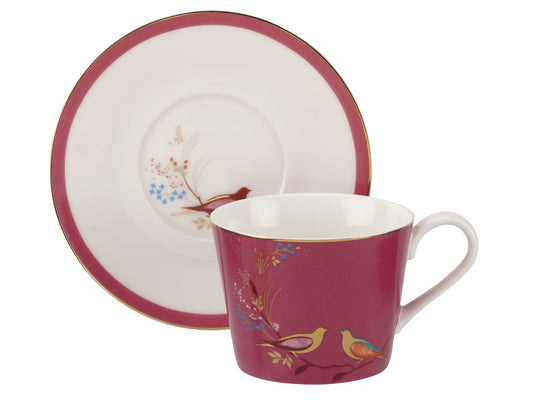 A white porcelain teacup and saucer, decorated with bright fuchsia pink rim on the saucer and background on the exterior of the mug, as well as gold detailing and two birds in delicate foliage