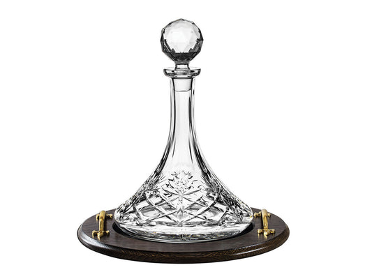A wide based cut crystal decanter with a long slim neck and a round stopper on a solid oak tray with gold handles