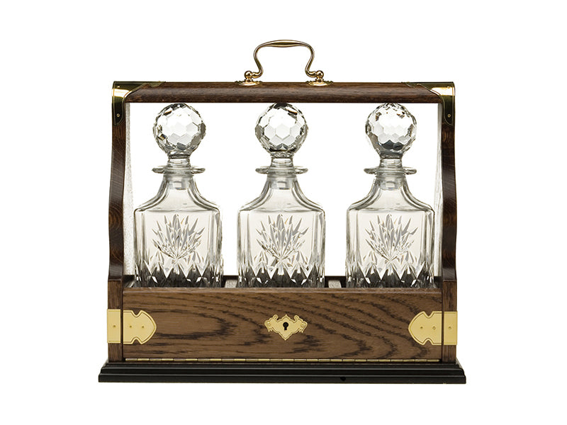 A set of three cut crystal decanters in a solid oak tantalus with gold details