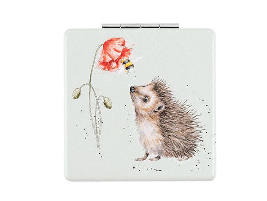 A light green square pocket mirror with a picture of a hedgehog looking at a bee on a poppy on the front.