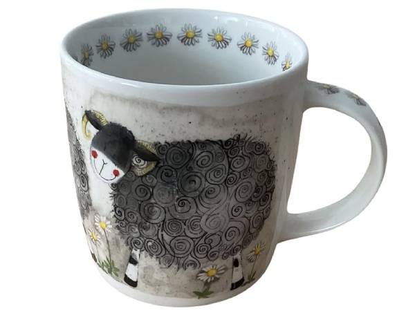 A white ceramic mug featuring a whimsical illustration of a black and white sheep with yellow daisies around it, shown against a plain white background.