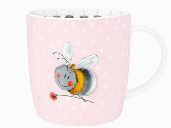 A light pink ceramic mug with a white handle, decorated with a pattern of small white hearts and a cute cartoon bumblebee holding a red flower.