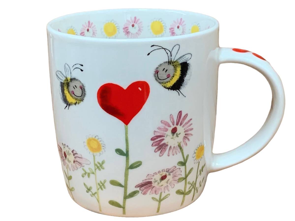 A white ceramic mug decorated with a whimsical design featuring two smiling bumblebees, a large red heart, and pink, yellow, and white flowers with green stems.