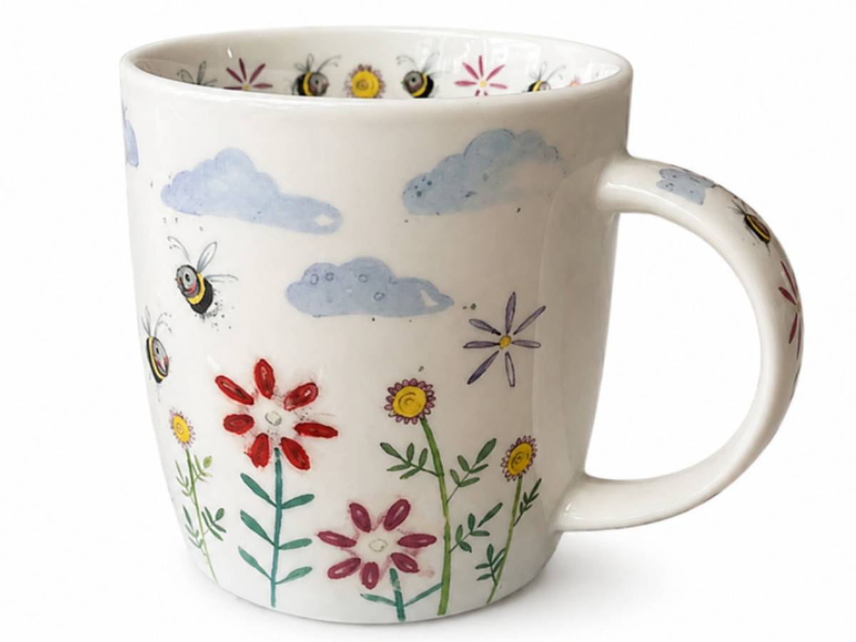 A white ceramic mug decorated with a whimsical pattern of blue clouds, yellow and red flowers, green stems, and bumblebees, shown against a plain white background.