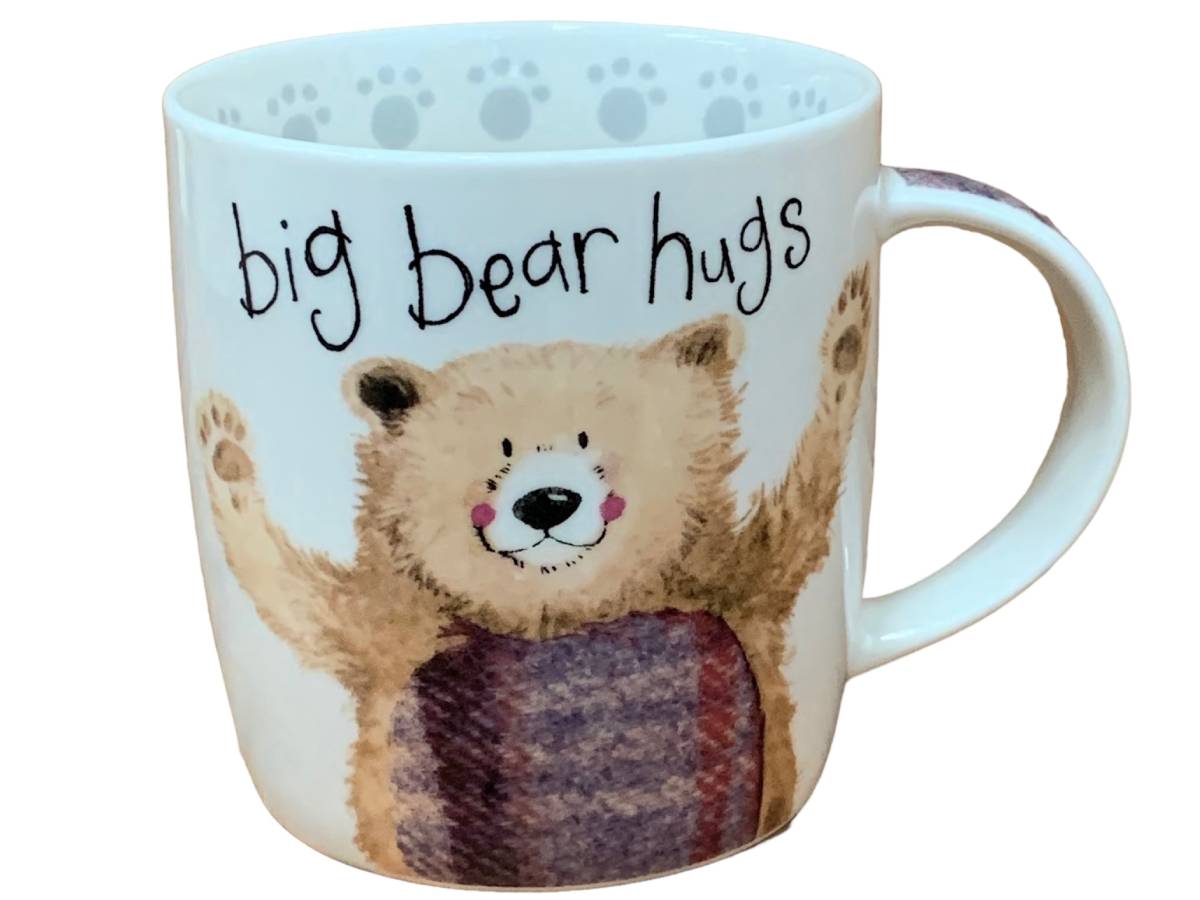 A white ceramic mug featuring a cute illustration of a bear hugging a child, with the text 'big bear hugs' written above. The bear is tan with a purple and red striped blanket, and the mug has a light blue paw print pattern on the inside rim.