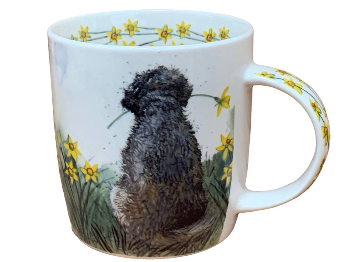 A white ceramic mug featuring a watercolor-style illustration of a black and brown dog holding yellow daffodils, with a border of yellow daffodils around the rim and handle.